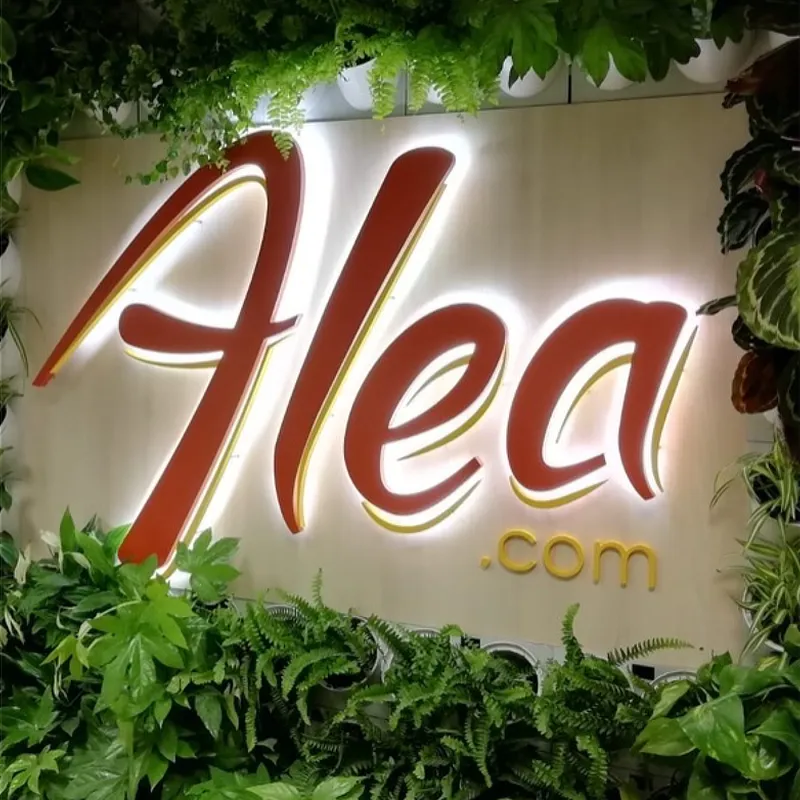 Rótulo iluminado de 'Alea.com' rodeado de abundante vegetación. El letrero presenta un diseño elegante con letras cursivas en rojo y amarillo, destacando en un entorno natural y atractivo, ideal para captar la atención de los clientes