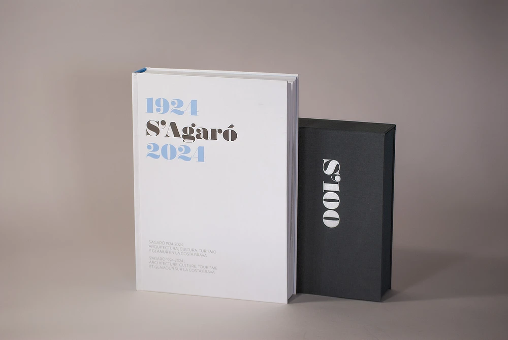 Libro conmemorativo "S’Agaró 1924-2024" en tapa dura blanca, acompañado de un estuche negro con letras en plata mate. Edición limitada de lujo que recorre la historia de este emblemático lugar de la Costa Brava.