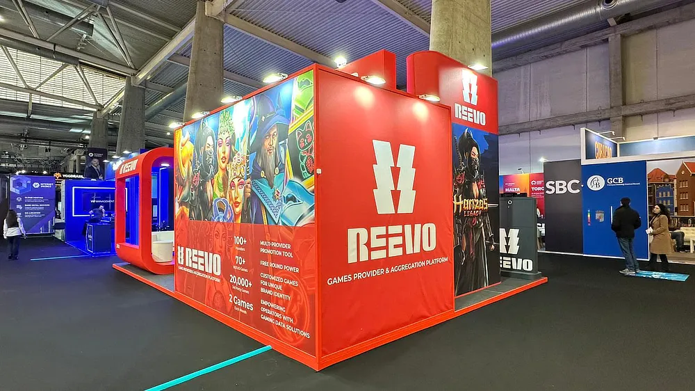 View of Reevo's stand at ICE 2025, featuring red panels, gaming character graphics, and prominent branding.