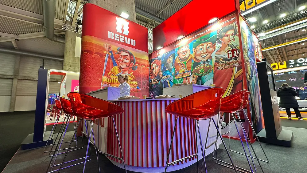 Bar area at Reevo's stand at ICE 2025 with red stools and graphics representing video game characters.