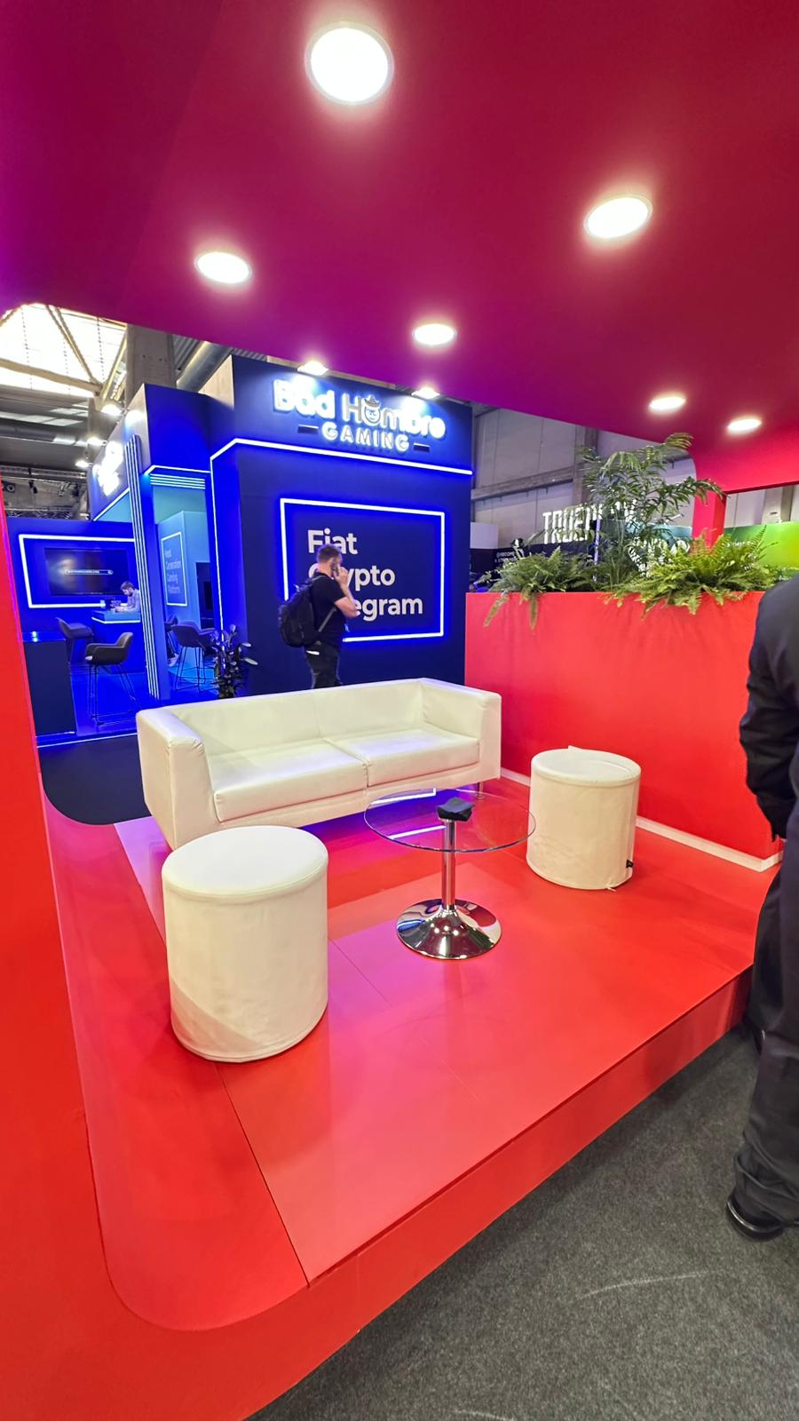 Lounge area at Reevo's stand at ICE 2025, featuring white sofas, a round table, and decorative greenery under warm lights.