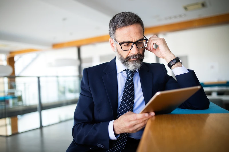 Hombre de negocios con barba y gafas usando una tableta digital en un entorno de oficina moderno.