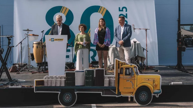 Stage with cardboard truck decor and De Rijke leadership giving speeches during the 80th anniversary event.