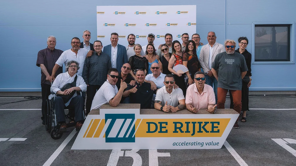 Photo de groupe avec employés et invités devant le photocall De Rijke sur le parking.