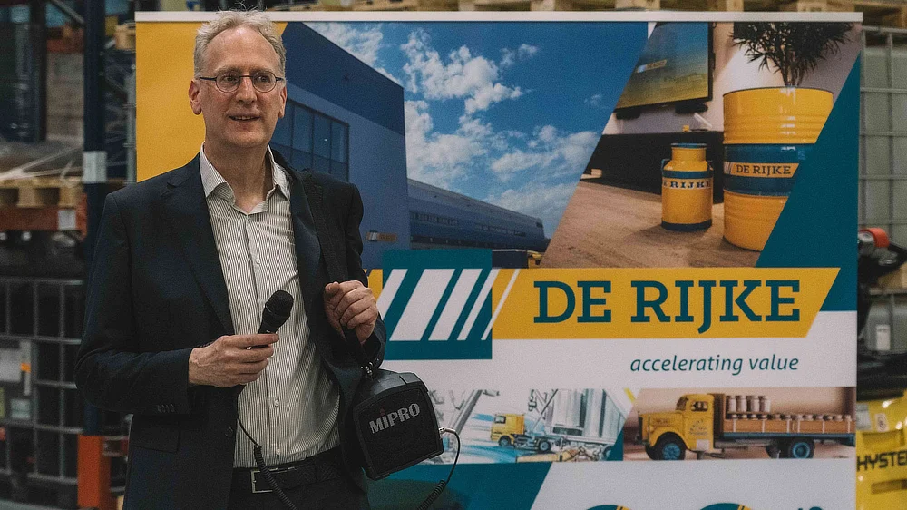 Représentant De Rijke avec micro devant un roll-up de communication de la marque.