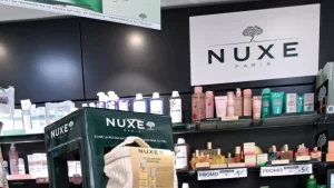 Upper detail of the Nuxe POS display in a pharmacy, showing the brand on top and cosmetic treatment kits placed on the front trays.