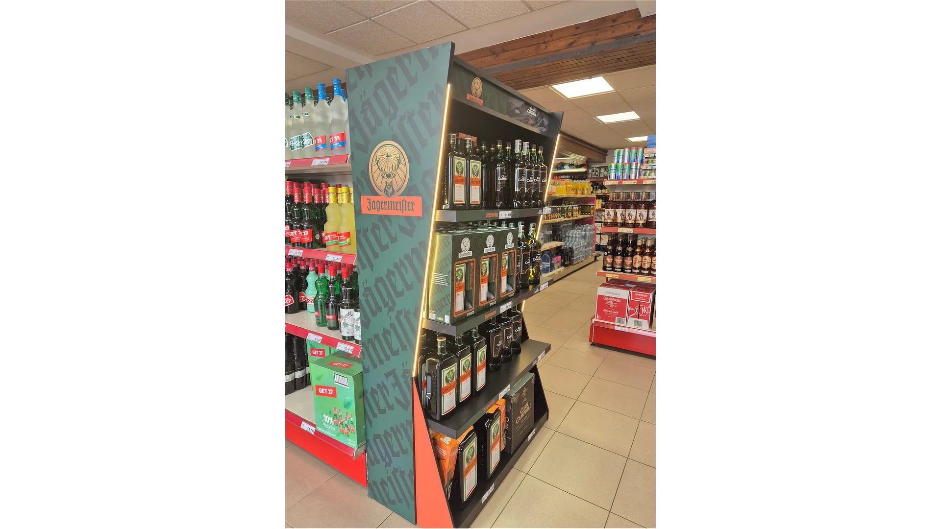 Vista lateral izquierda de la cabecera de PLV mixta para Great Spirit, mostrando botellas, gráficas renovables y estructura iluminada en un pasillo de supermercado.