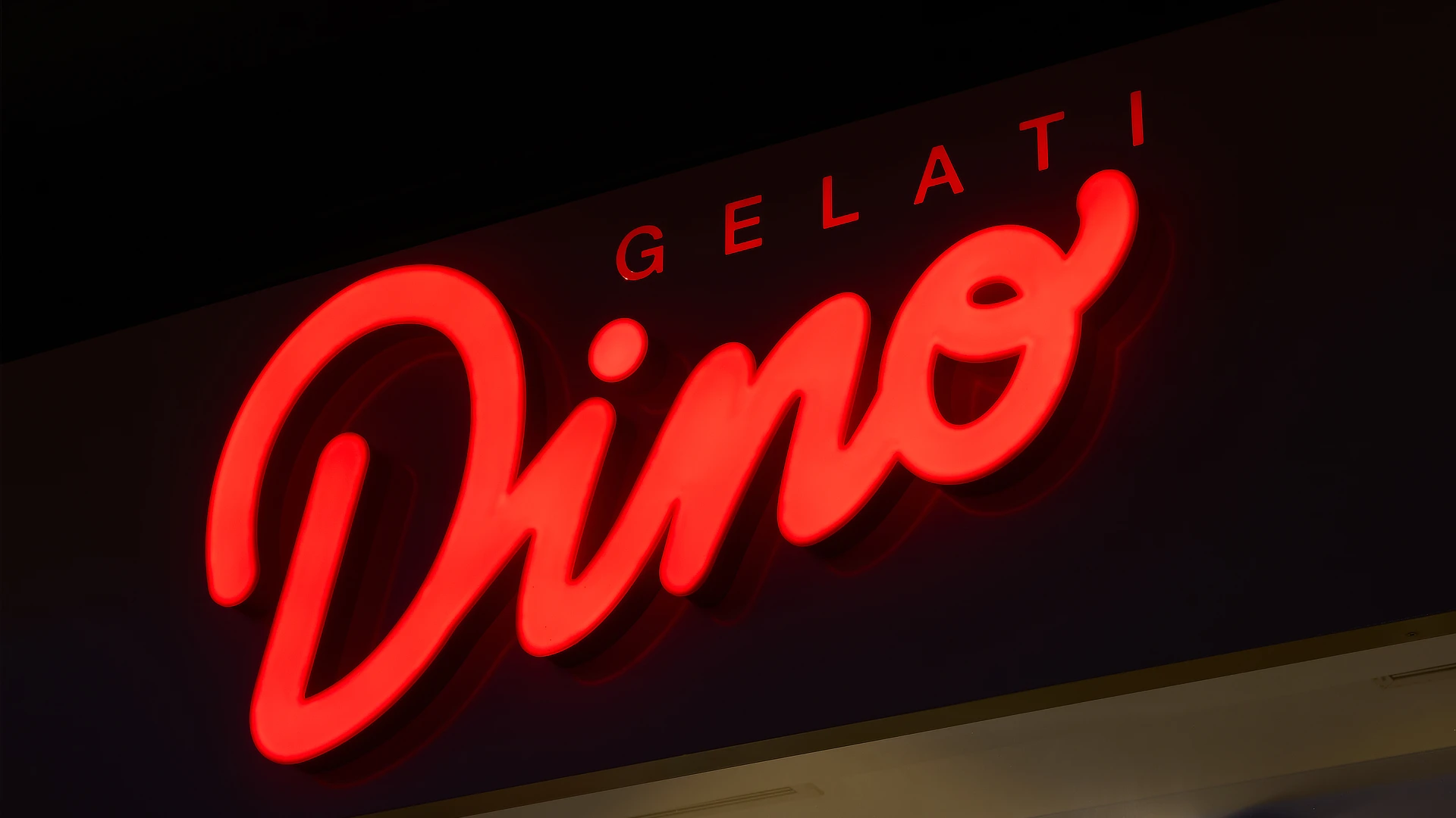 Primer plano del rótulo rojo retroiluminado “Dino” sobre fondo oscuro, mostrando el brillo y volumen del corpóreo luminoso.