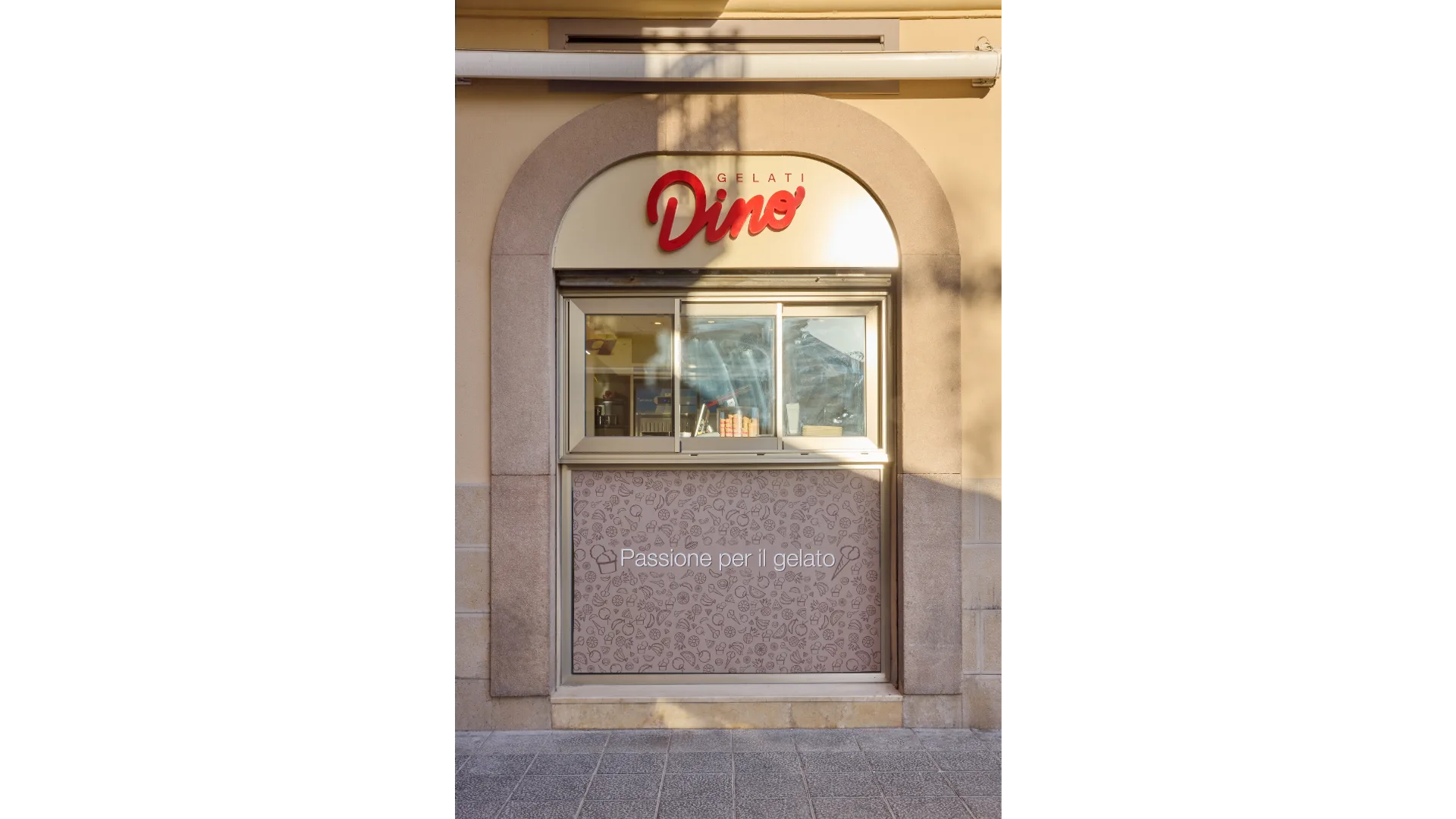 Ventana de despacho de helados Dino con rótulo rojo retroiluminado y vinilo inferior decorativo con el texto “Passione per il gelato”.