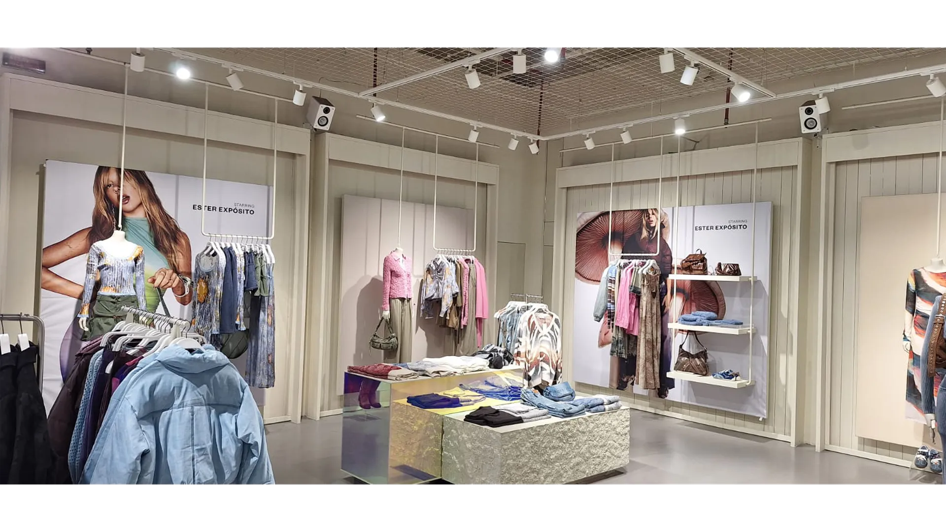 Imagen interior de tienda Desigual con paneles de campaña gran formato Desigual, mostrando fotografías de Ester Expósito y racks de ropa integrados en una instalación visual sostenible.