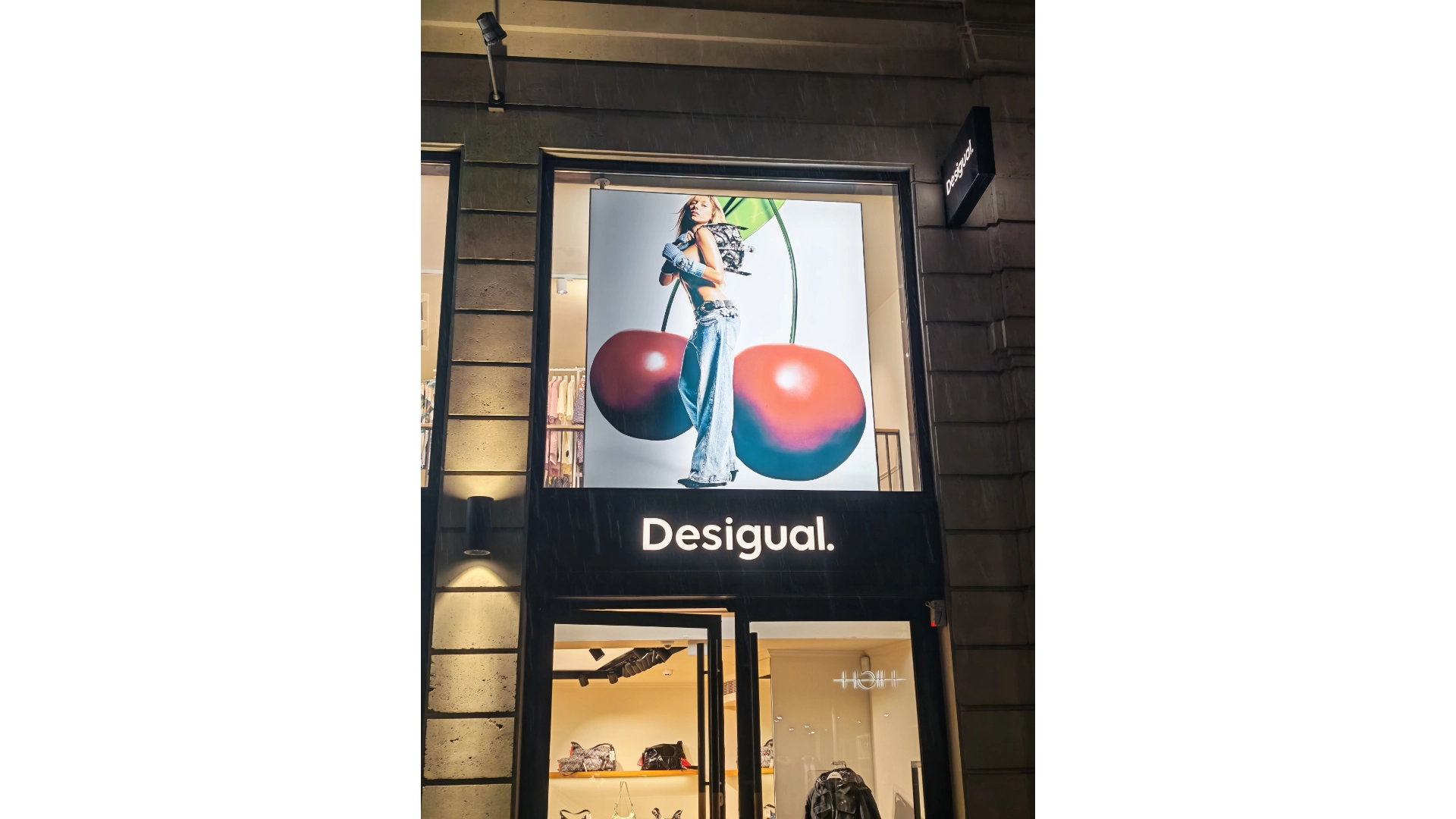 Imagen exterior de tienda Desigual con creatividad de campaña gran formato Desigual, mostrando a Ester Expósito en un panel iluminado situado sobre el acceso principal.
