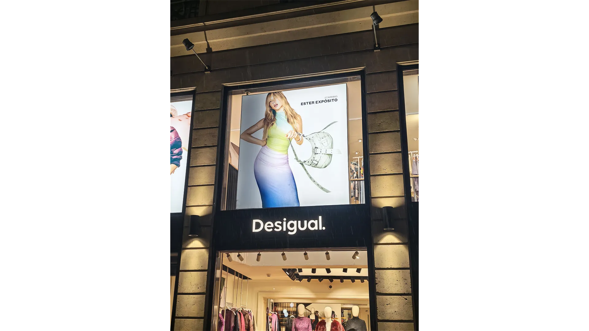 Fachada de tienda Desigual con tres grandes paneles de campaña gran formato Desigual, cada uno con imágenes distintas de Ester Expósito y creatividad visual destacada.