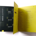 Páginas interiores de una memoria anual abiertas, mostrando un índice bilingüe y secciones corporativas diseñadas con una maquetación moderna en tonos negros y amarillos.
