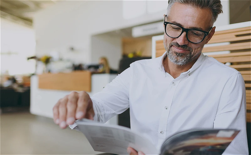 Hombre hojeando una memoria anual en un entorno profesional, simbolizando la lectura y aprovechamiento de contenidos corporativos.