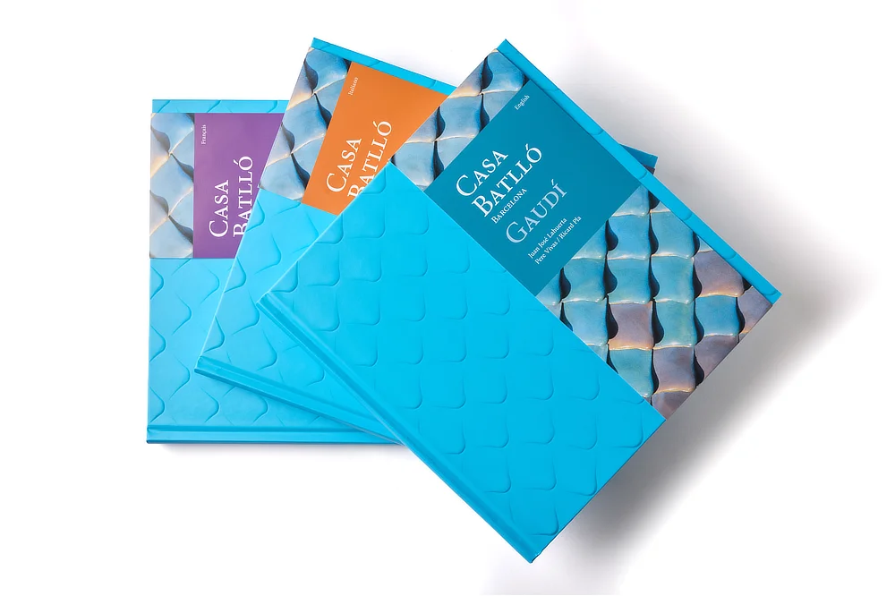 Conjunto de tres ejemplares del libro de arte Casa Batlló apilados, mostrando las fajas verticales de colores que diferencian las ediciones en varios idiomas.