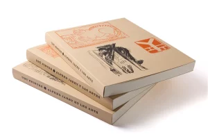 Tres exemplars del llibre d'art Alfred Jarry apilats, mostrant els lloms en català, castellà i francès sobre un fons blanc net.