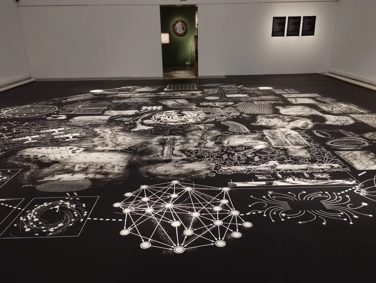 Perspectiva amplia de la sala con el vinilo de suelo para el Centre d’Arts Santa Mònica mostrando diagramas de redes y dibujos anatómicos detallados.