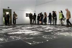 Visitantes caminando sobre el vinilo de suelo de grandes dimensiones con ilustraciones científicas y esquemas en blanco sobre fondo negro en la sala de exposición.