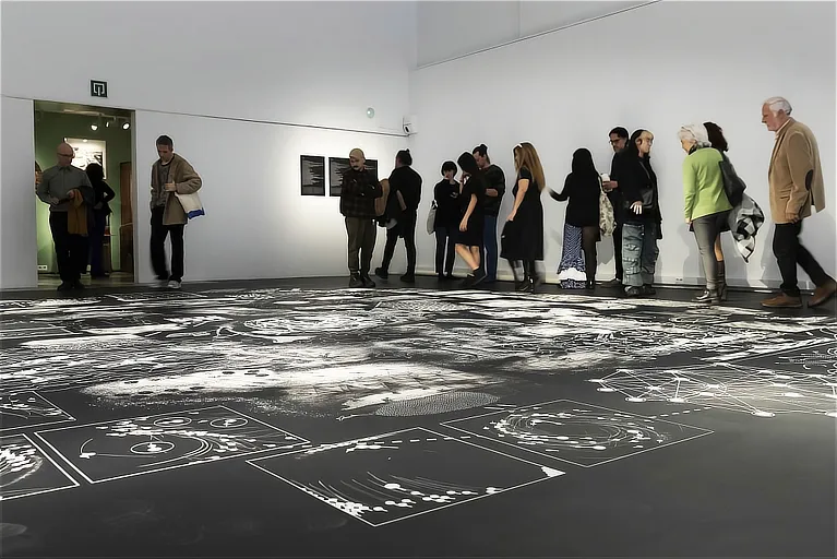 Visiteurs marchant sur le sol vinyle de grandes dimensions avec des illustrations scientifiques et des schémas blancs sur fond noir dans la salle d'exposition.