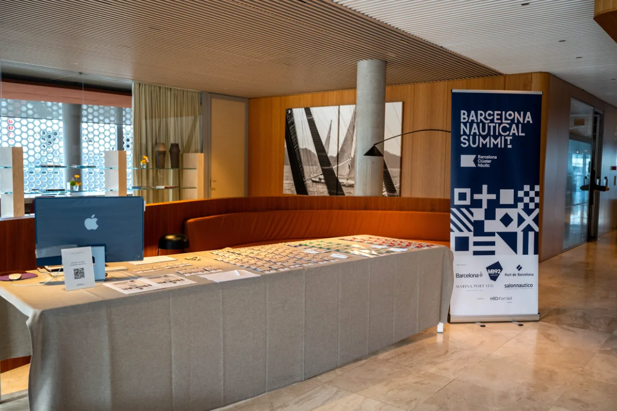 Zona de acreditaciones con mesa de registro, materiales impresos y roll-up de gran formato Barcelona Nautical Summit reforzando la identidad visual del evento.
