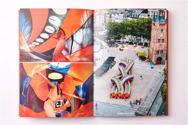 Libro de arte abierto mostrando una composición fotográfica a color en páginas interiores que retrata una instalación inflable de color naranja y azul en una plaza pública.